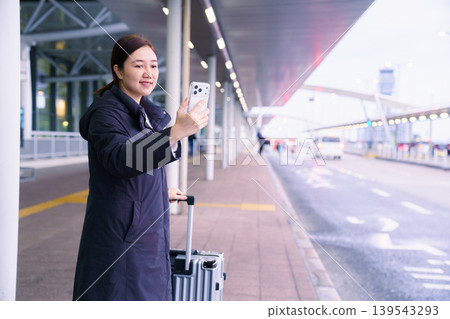 Asian female traveler with luggage taking selfie or video call at airport bus stop Asian female traveler with luggage taking selfie or video call at airport bus stop 139543293