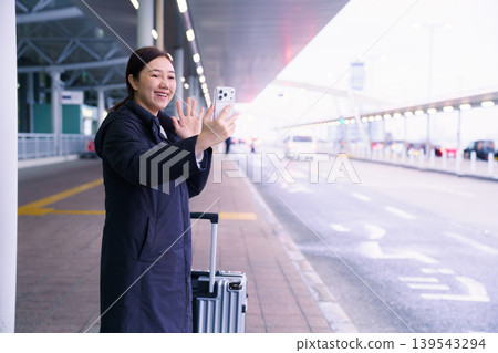 Asian female traveler with luggage taking selfie or video call at airport bus stop Asian female traveler with luggage taking selfie or video call at airport bus stop 139543294