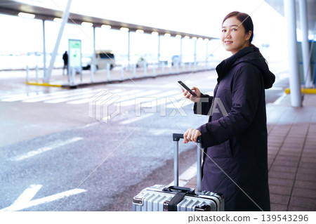 Asian woman with suitcase using smartphone at airport Asian woman with suitcase using smartphone at airport 139543296
