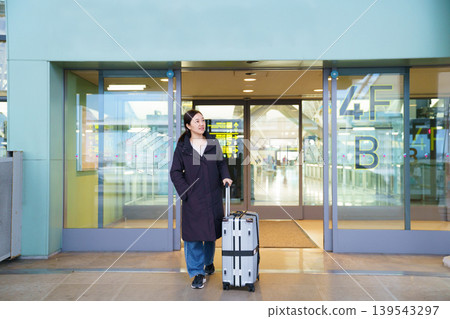 Asian woman with suitcase at airport terminal entrance Asian woman with suitcase at airport terminal entrance 139543297