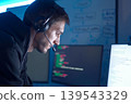 Software developer analyzing code on computer monitors while wearing headset in dark workspace 139543329