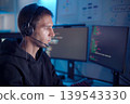 Software developer analyzing code on computer monitors while wearing headset in dark workspace 139543330