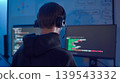 Software developer wearing headset reviewing program code on monitor in low light workspace 139543332