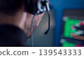 Software developer wearing headset reviewing program code on monitor in low light workspace 139543333