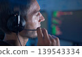 Software developer analyzing code on computer monitors while wearing headset in dark workspace 139543334