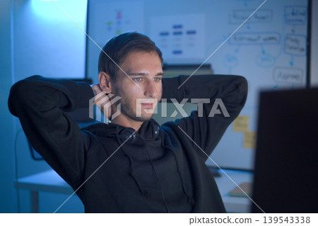 Software developer relaxing after solving programming problem while working at computer workstation 139543338