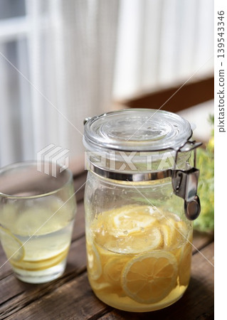 A bottle of homemade lemon syrup and hot lemonade placed on the windowsill. 139543346