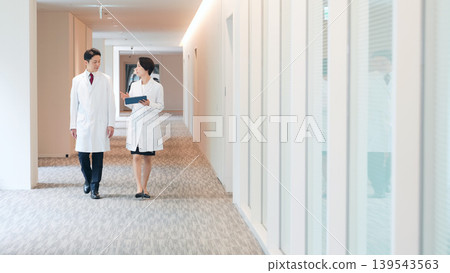 A group of men and women in white coats walking through the office A group of men and women in white coats walking through the office 139543563