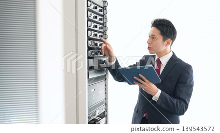 A male engineer inspecting a server. 139543572
