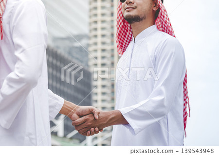 Islamic businessman shake hands together dealing success business in modern muslim UAE city. Arab man wear hijab muslim dress. Multicultural diversity business people meeting talking group cityscape Islamic businessman shake hands together dealing success business in modern muslim UAE city. Arab man wear hijab muslim dress. Multicultural diversity business people meeting talking group cityscape 139543948