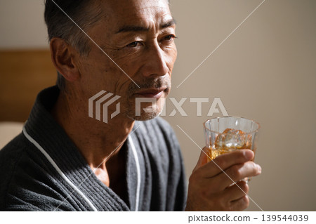 Senior man wearing a gown and holding a rocks glass Lifestyle image Senior man wearing a gown and holding a rocks glass Lifestyle image 139544039