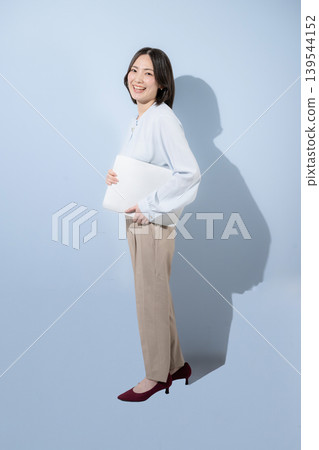 一位面帶微笑的女性手持筆記型電腦，背景是淺藍色背景，這代表著積極、可愛、值得信賴、自信，為求職和招聘提供了令人耳目一新的形象。 139544152