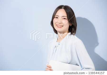 一位女性以淺藍色背景為襯托,手持筆記型電腦,對著鏡頭微笑,傳遞出積極、可愛、信任和自信的訊息——適合求職和招募。 一位女性以淺藍色背景為襯托,手持筆記型電腦,對著鏡頭微笑,傳遞出積極、可愛、信任和自信的訊息——適合求職和招募。 139544157