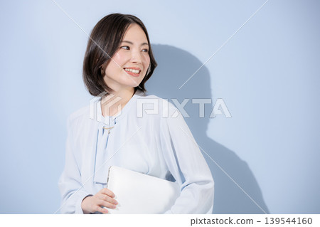 一張積極向上的肖像照,照片中一位面帶微笑的女性手持筆記型電腦,背景是淺藍色,展現出一位酷女性的自信和沈穩。 一張積極向上的肖像照,照片中一位面帶微笑的女性手持筆記型電腦,背景是淺藍色,展現出一位酷女性的自信和沈穩。 139544160