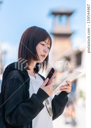 A young Japanese woman enjoys sightseeing in Kawagoe, checking a map on her smartphone. Travel, strolling, lifestyle. A young Japanese woman enjoys sightseeing in Kawagoe, checking a map on her smartphone. Travel, strolling, lifestyle. 139544967