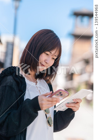 一位年輕的日本女性在川越觀光,一邊用智慧型手機查看地圖。旅行、漫步、生活方式。 一位年輕的日本女性在川越觀光,一邊用智慧型手機查看地圖。旅行、漫步、生活方式。 139544968