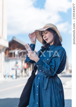 A woman in a straw hat is sightseeing in Koedo Kawagoe, looking at a map on her smartphone. She is walking around town and traveling. 139544977