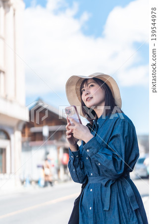 A woman in a straw hat is sightseeing in Koedo Kawagoe, looking at a map on her smartphone. She is walking around town and traveling. 139544978