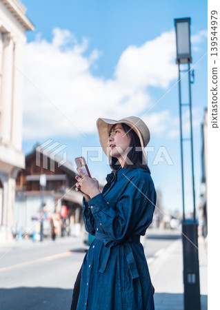 A woman in a straw hat is sightseeing in Koedo Kawagoe, looking at a map on her smartphone. She is walking around town and traveling. A woman in a straw hat is sightseeing in Koedo Kawagoe, looking at a map on her smartphone. She is walking around town and traveling. 139544979