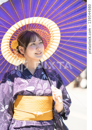 A woman in a yukata (summer kimono) and carrying a traditional Japanese umbrella enjoys sightseeing in the historic town of Kawagoe, a summer travel destination, strolling through the historic storehouse-lined streets. A woman in a yukata (summer kimono) and carrying a traditional Japanese umbrella enjoys sightseeing in the historic town of Kawagoe, a summer travel destination, strolling through the historic storehouse-lined streets. 139544980