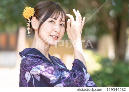 A Japanese woman smiling in a yukata (summer kimono). Summer portrait. Navy blue yukata, hair ornament, green background. A Japanese woman smiling in a yukata (summer kimono). Summer portrait. Navy blue yukata, hair ornament, green background. 139544982