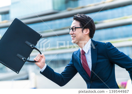 A businessman runs through the office district with his bag in hand and a smile on his face. 139544987