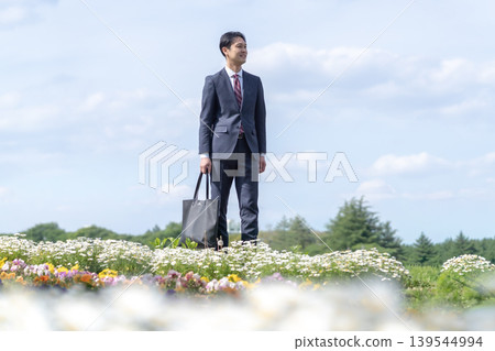 一位身穿西裝的男子凝視著遠方的花田。 一位身穿西裝的男子凝視著遠方的花田。 139544994