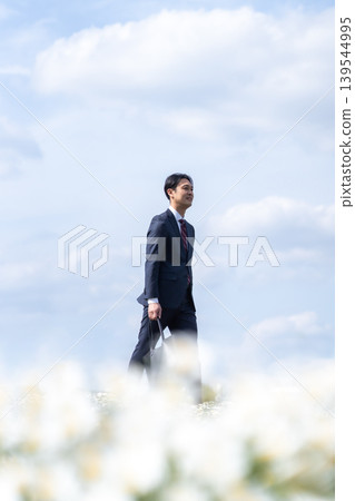 A man in a suit gazes into the distance in a flower field bathed in spiritual light. A man in a suit gazes into the distance in a flower field bathed in spiritual light. 139544995