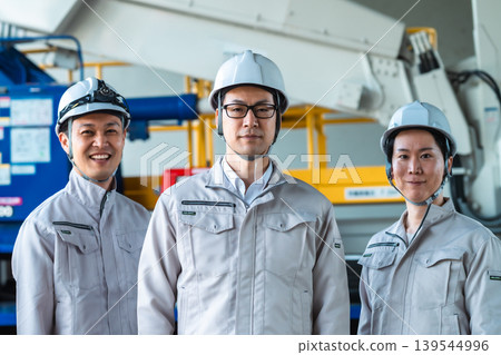 Three male staff members in work clothes standing side by side at a factory or construction site. Three male staff members in work clothes standing side by side at a factory or construction site. 139544996