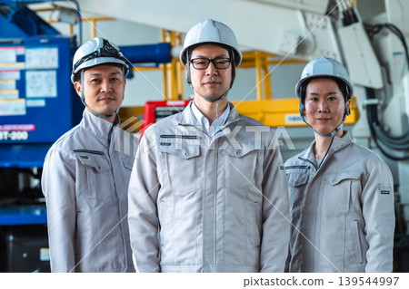 Three male staff members in work clothes standing side by side at a factory or construction site. Three male staff members in work clothes standing side by side at a factory or construction site. 139544997