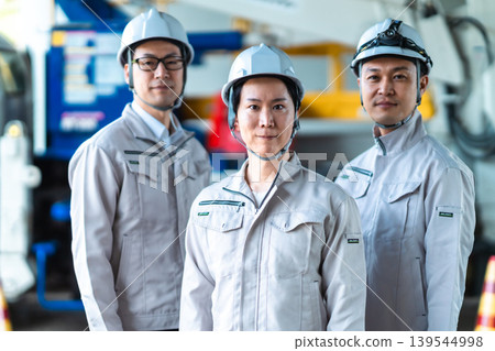 Three male staff members in work clothes standing side by side at a factory or construction site. 139544998