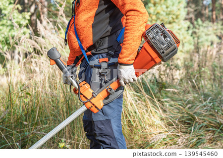 Brush cutter operator with grass trimmer for landscaping and lawn maintenance in a field Brush cutter operator with grass trimmer for landscaping and lawn maintenance in a field 139545460