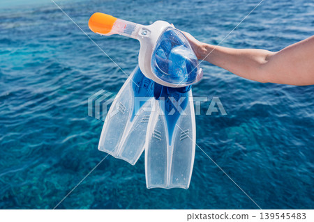 Snorkeling gear mask and fins held over the blue ocean water in the Caribbean islands Snorkeling gear mask and fins held over the blue ocean water in the Caribbean islands 139545483