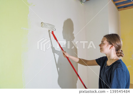Young woman painting interior wall with roller, home improvement and renovation project Young woman painting interior wall with roller, home improvement and renovation project 139545484