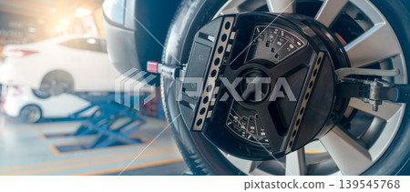 Wheel alignment equipment grip the tire of car wheel in car repair shop. Auto wheel alignment in workshop of service station. Car wheel balance. Suspension adjustment. Vehicle inside garage workshop. 139545768