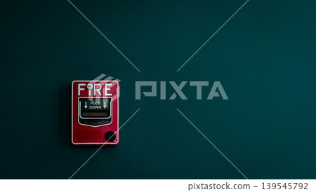 Fire alarm on dark green concrete wall. Warning and security system. Emergency equipment for safety alert. Red box of fire alarm on wall of school, hospital, factory, office, apartment, or home. 139545792