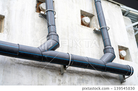 Polyethylene pipes drain water from sky train tracks. HDPE pipeline drainage. Black PE tube was installed on a building wall. Polyethylene pipe network. Pipe construction. Water drainage HDPE pipe. Polyethylene pipes drain water from sky train tracks. HDPE pipeline drainage. Black PE tube was installed on a building wall. Polyethylene pipe network. Pipe construction. Water drainage HDPE pipe. 139545830