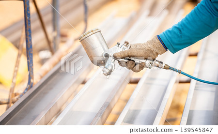 Construction worker painting metal structure surface coating with a spray gun at construction site. Metal corrosion and rust protection. Industrial precision. Protective coating to a metal structure. 139545847