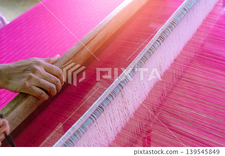 Woman working on weaving machine for weave handmade fabric. Textile weaving. Weaving using traditional hand weaving loom on the long cotton strands. Textile production in Thailand. Asian culture. Woman working on weaving machine for weave handmade fabric. Textile weaving. Weaving using traditional hand weaving loom on the long cotton strands. Textile production in Thailand. Asian culture. 139545849