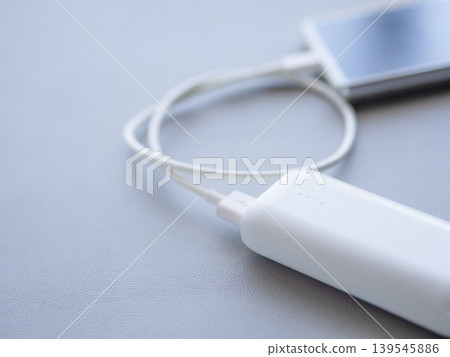A smartphone charging with a white mobile battery. 139545886