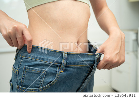 Young Asian woman losing weight wearing loose pants in oversize jeans. Young Asian woman losing weight wearing loose pants in oversize jeans. 139545911