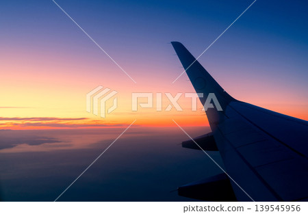 Wing of plane with sunrise skyline. Airplane flying in the sky. Scenic view from airplane window. Commercial airline flight. Plane wing above clouds. International flight. Travel abroad after covid-19 Wing of plane with sunrise skyline. Airplane flying in the sky. Scenic view from airplane window. Commercial airline flight. Plane wing above clouds. International flight. Travel abroad after covid-19 139545956
