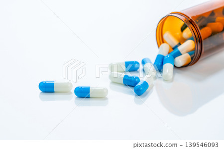 Prescription antibiotic capsules spilling from amber bottle onto a white background. Blue and white capsule pills. Ideal for healthcare, pharmaceutical treatments, and medical medication industries. Prescription antibiotic capsules spilling from amber bottle onto a white background. Blue and white capsule pills. Ideal for healthcare, pharmaceutical treatments, and medical medication industries. 139546093