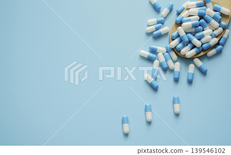 Blue and white antibiotic capsule pill and wooden spoon on blue background. Pills frame with space. Antibiotic drugs. Pharmaceutical industry. Pharmacology. Healthcare and medical care concept. Blue and white antibiotic capsule pill and wooden spoon on blue background. Pills frame with space. Antibiotic drugs. Pharmaceutical industry. Pharmacology. Healthcare and medical care concept. 139546102