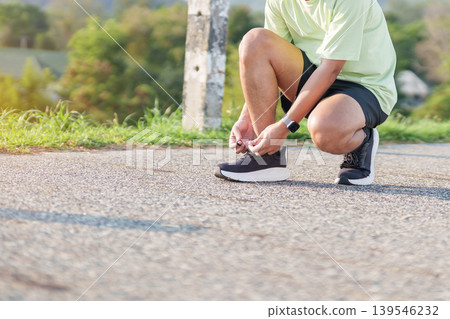Young Asian man tying running shoes in the park. Female runner getting ready for jogging and exercise on the road. Fitness, wellness and outdoor sport concept in morning 139546232