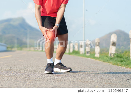 Young adult male runner with knee pain from ACL injury or patellofemoral syndrome. Man having joint ache, ligament tear or patellar tendinitis during running. Sports medical and healthcare concept Young adult male runner with knee pain from ACL injury or patellofemoral syndrome. Man having joint ache, ligament tear or patellar tendinitis during running. Sports medical and healthcare concept 139546247