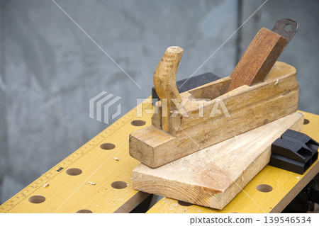 Vintage wooden hand plane resting on a workbench with lumber and measuring tool Vintage wooden hand plane resting on a workbench with lumber and measuring tool 139546534