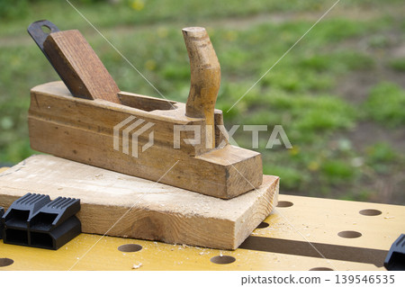 Vintage wooden hand plane resting on a workbench with wood shavings Vintage wooden hand plane resting on a workbench with wood shavings 139546535
