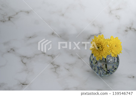 A single yellow chrysanthemum in a cool-toned glass sphere vase against a bright background (placed on the right). A single yellow chrysanthemum in a cool-toned glass sphere vase against a bright background (placed on the right). 139546747
