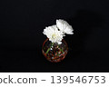 A single white chrysanthemum (centered) in a cool-toned, glass-sphere-shaped vase floating in the darkness. A single white chrysanthemum (centered) in a cool-toned, glass-sphere-shaped vase floating in the darkness. 139546753